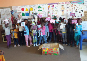 Zdjecie przedstawia grupę dzieci z Afryki przed którymi znajduje się paczka, która dotarła dla nich z Polski od naszych przedszkolaków.